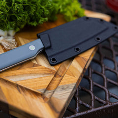 Leatherman Rustle in sheath placed on a cutting board alongside a selection of vibrant vegetables, indicating meal preparation.