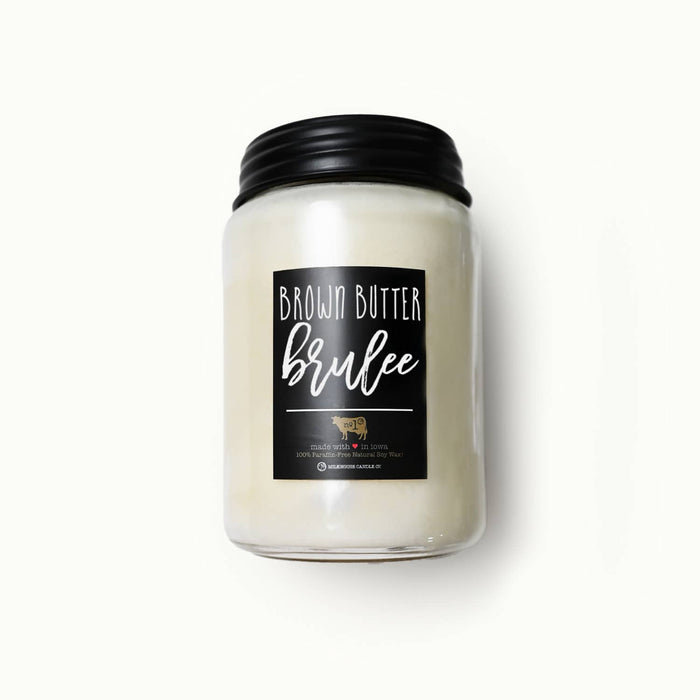 A jar candle with creamy off-white wax in a clear glass jar, featuring a black metal lid and a black label that reads 'BROWN BUTTER brulee'.