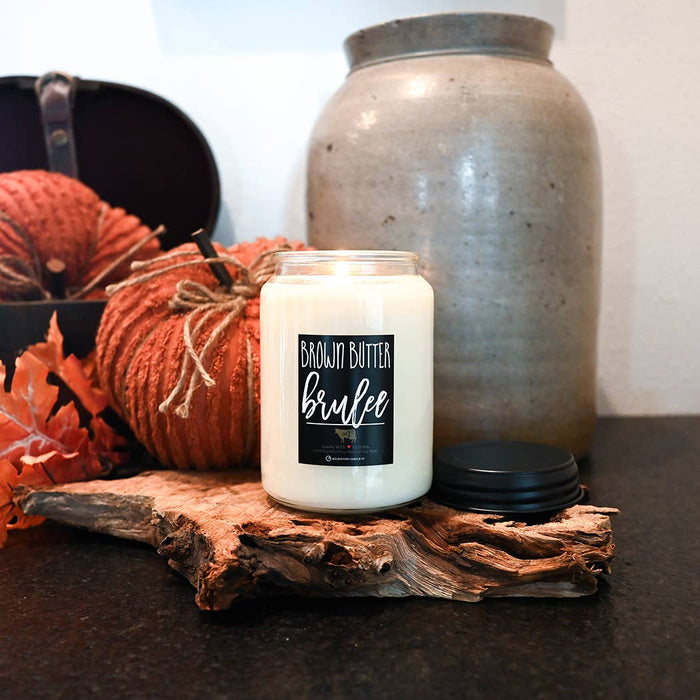 Candle labeled 'Brown Butter Brulee' on a wooden surface with pumpkins and a ceramic jar in the background.