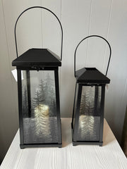 Two black LED candle lanterns with glass panels that have trees.