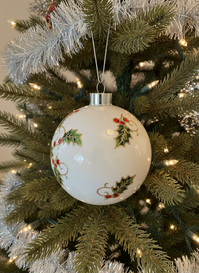 A decorative glass ball ornament with a Christmas design, encased in a cardboard box with a silver foil lining.