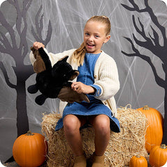 Child holding a stuffed animal in front of a Halloween-themed backdrop with pumpkins and hay.