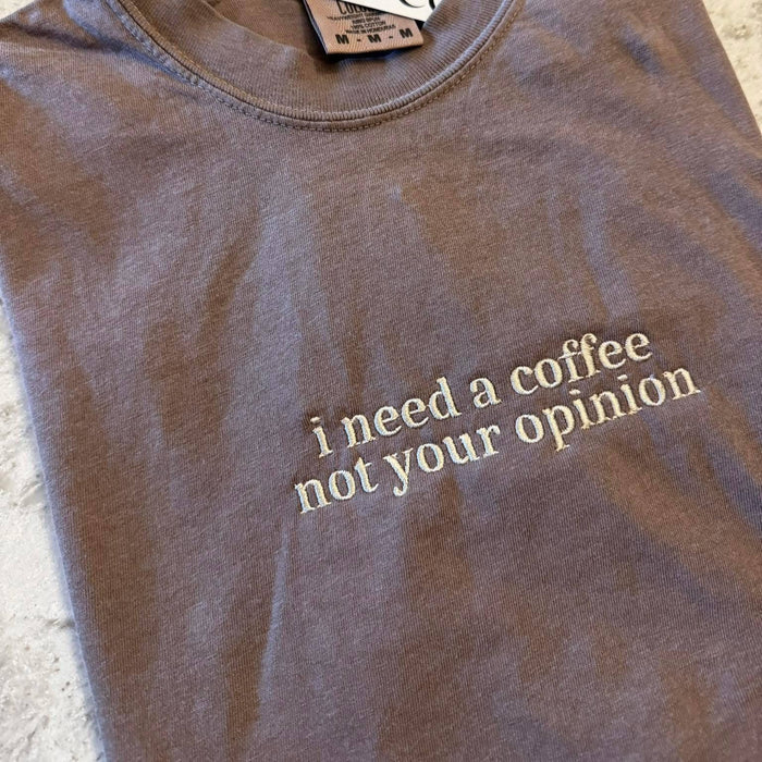 Brown t-shirt with text 'i need a coffee not your opinion' on a textured surface