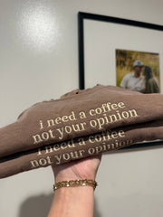 Folded brown sweatshirt with text held by a hand, framed photo in the background