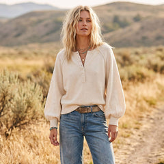 Woman standing in a desert landscape wearing a beige blouse and blue jeans.