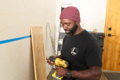 A person wearing a black Leatherman Classic Tee holding a yellow power drill while working indoors.