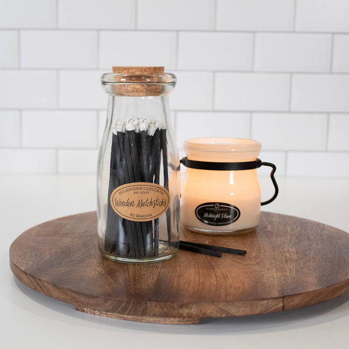Jar of matches and candle on a wooden board with white tiled background