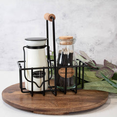 Wooden tray with a black metal bottle holder containing a milk bottle and a glass jar on a light background.