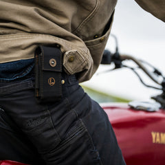 A man riding a motorcycle, wearing the Leatherman Black Bronze Nylon Sheath on his side, cruising down a scenic road.