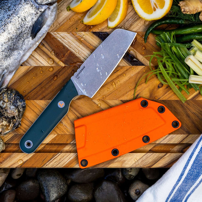 Leatherman Rustle Knife and sheath on block beside a colorful assortment of fresh vegetables on a wooden cutting board.