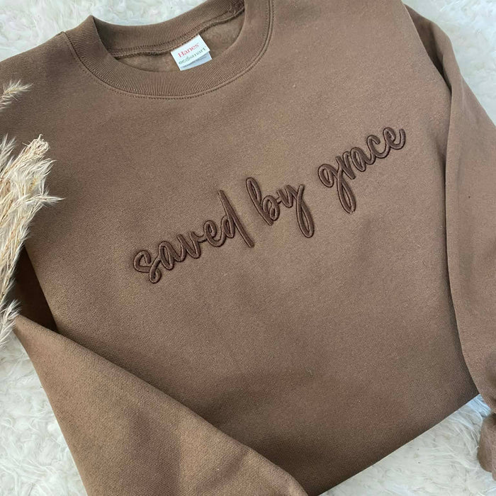 Brown sweatshirt with 'saved by grace' text on a textured surface