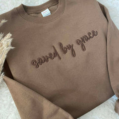 Brown sweatshirt with 'saved by grace' text on a textured surface