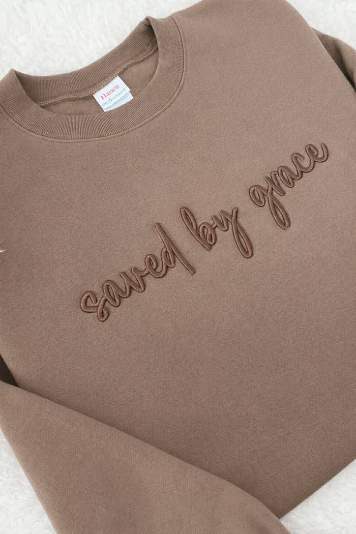 Brown sweatshirt with 'saved by grace' text on a light gray background