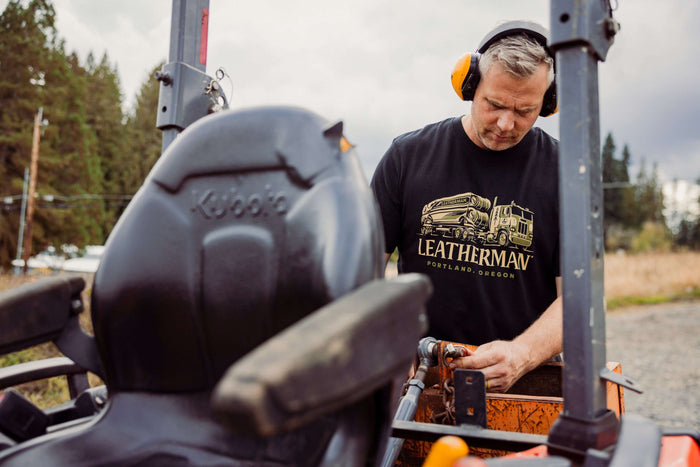 A person wearing a black Leatherman Timber Tee working on a tractor outdoors.