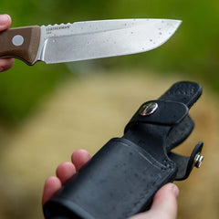 Earth Brown Leatherman Trac Knife with water drops on the blade held in one hand, while the Leatherman Trac Knife Sheath with silver snap closures open held in the other hand.