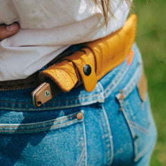 Earth Brown Leatherman Trac Knife handle sticking out of a Brown Leatherman Trac Knife Sheath with black snap closures that is attached to the back of a woman's belt.